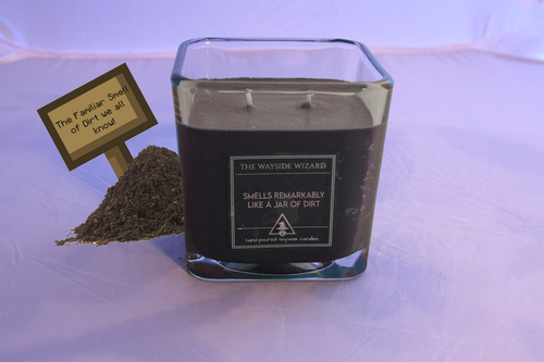 a brown 22oz jar of dirt themed dnd candle from the Wayside Wizard. There is a pile of dirt and a pixelated sign to the left of the jar. The sign says 